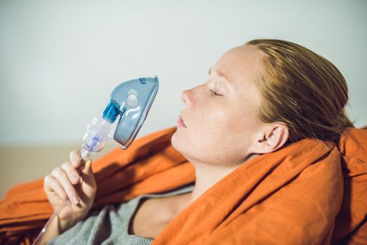 Woman with flu or cold symptoms making inhalation with nebulizer - medical inhalation therapy.