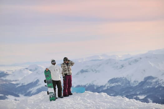 happy young snowboarder couple relax at top of mountain at beautiful sunny winter day