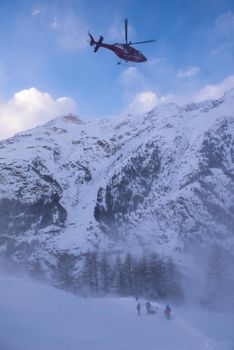 a rescue team with a red helicopter performing the action of rescuing a hurt skier on ski resort
