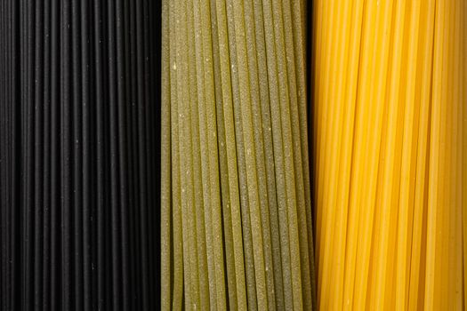 Colored spaghetti raw dry set, on black dark stone table background, top view flat lay