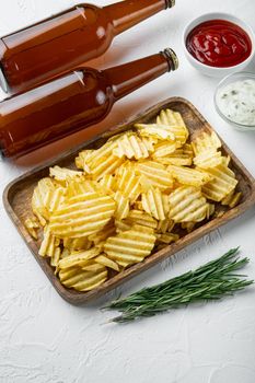 Delicious crispy potato chips set, with dipping sauces tomato dip sour cream, and bottle of beer, on white stone surface