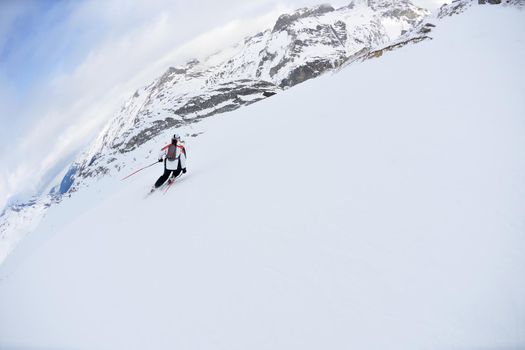 skier skiing downhill on fresh powder snow  with sun and mountains in background