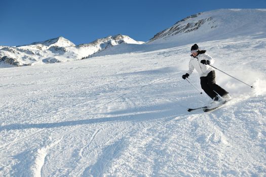 skier skiing downhill on fresh powder snow  with sun and mountains in background