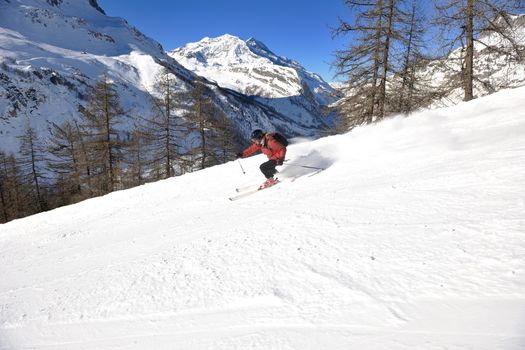 skier skiing downhill on fresh powder snow  with sun and mountains in background