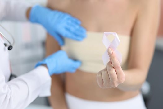 Doctor gynecologist examining patient breast with pink tape closeup. Breast cancer day concept