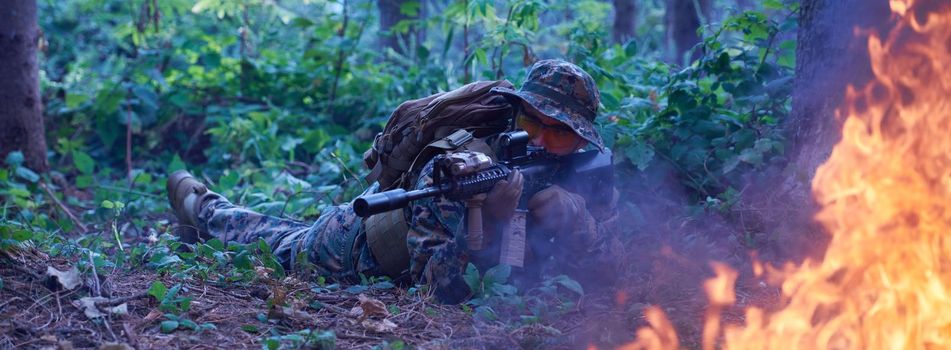 modern warfare soldier in action aiming at weapon  laser sight optics  in combat position while searching for a target in battle