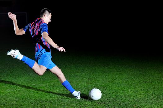 soccer player doing kick with ball on football stadium  field  isolated on black background  in night