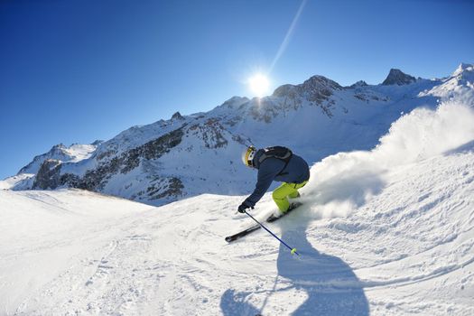 skier skiing downhill on fresh powder snow  with sun and mountains in background