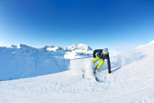 skier skiing downhill on fresh powder snow  with sun and mountains in background