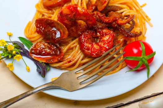 Italian seafood spaghetti pasta on red tomato sauce over white rustic wood table