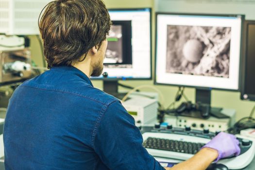 Scientist works at a electron microscope control pannel with two monitors in front of him.