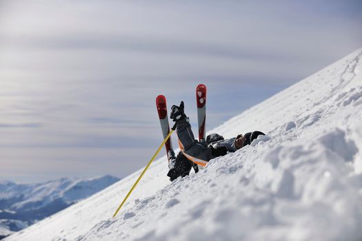 young skier relaxing in snow and looking mountain range at beautiful sunny winter day