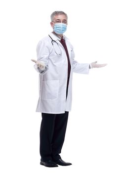 in full growth. a strict doctor in a protective mask pointing at you. isolated on a white background.