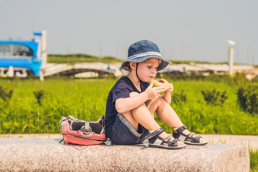A boy eats his snack on a park bench.