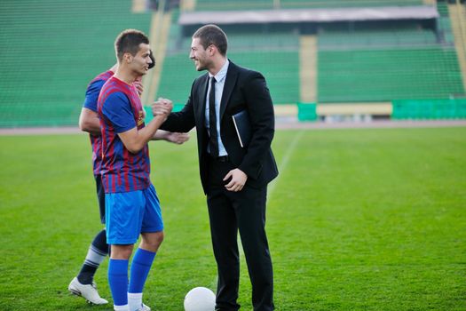 soccer  sport manager in business suit coach and football player on stadium with green grass and white ball