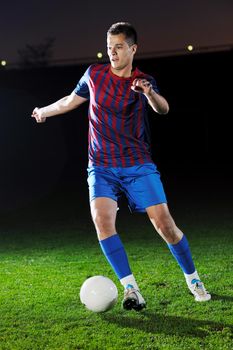 soccer player doing kick with ball on football stadium  field  isolated on black background  in night