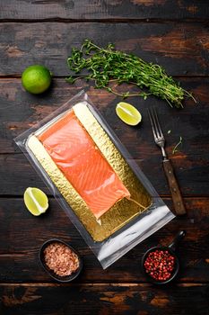 Piece of salmon fillets in a vacuum blister pack set, with herbs, on old dark wooden table background, top view flat lay