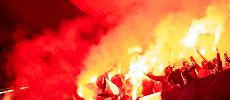 football hooligans with mask holding torches in fire while supporting their favorite team during a match at stadium