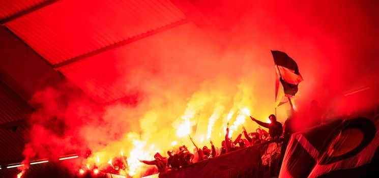 football hooligans with mask holding torches in fire while supporting their favorite team during a match at stadium