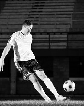 soccer player doing kick with ball on football stadium  field  isolated on black background  in night