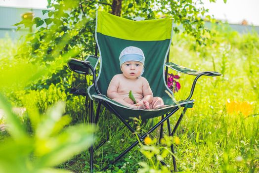 Cute blond baby boy enjoying the sun sitting on chair in a garden.