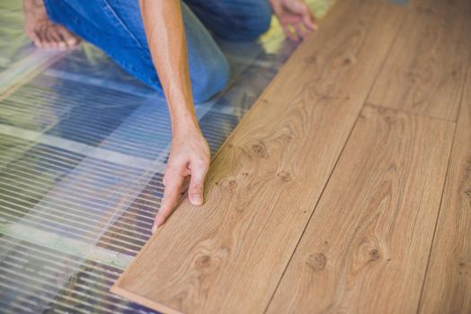 Man installing new wooden laminate flooring on a warm film floor. infrared floor heating system under laminate floor