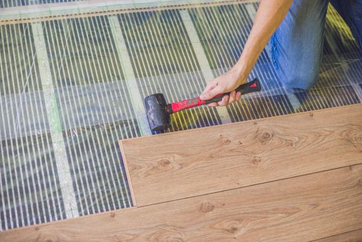 Man installing new wooden laminate flooring on a warm film floor. infrared floor heating system under laminate floor