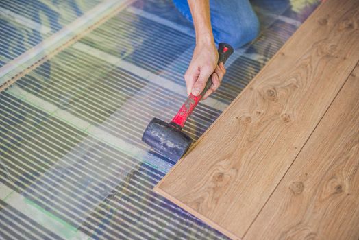 Man installing new wooden laminate flooring on a warm film floor. infrared floor heating system under laminate floor