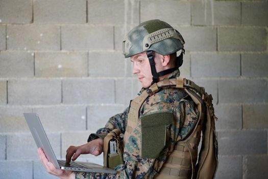 American soldier in military uniform using laptop computer for drone controlling and to stay in contact with friends and family