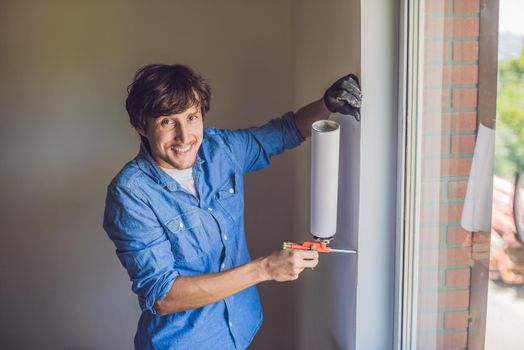 Man in a blue shirt does window installation. Using a mounting foam.