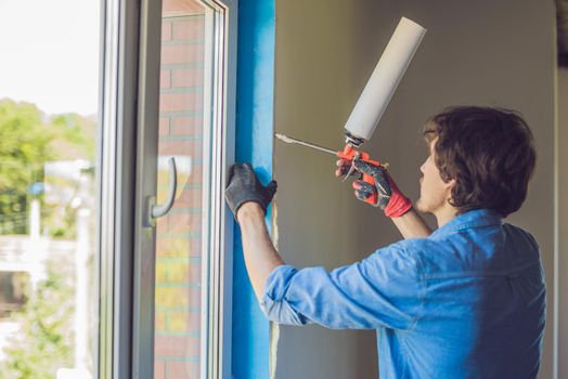 Man in a blue shirt does window installation. Using a mounting foam.