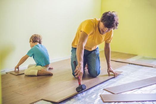 Father and son installing new wooden laminate flooring on a warm film floor. infrared floor heating system under laminate floor