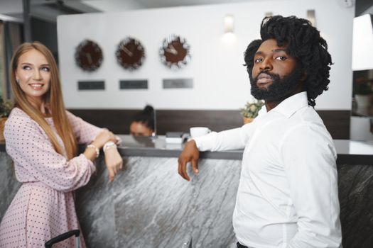 Business trip concept. Black man and caucasian woman businesspeople colleagues checking-in in hotel reception desk