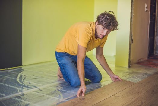 Man installing new wooden laminate flooring on a warm film floor. infrared floor heating system under laminate floor