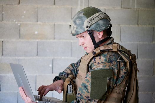 American soldier in military uniform using laptop computer for drone controlling and to stay in contact with friends and family