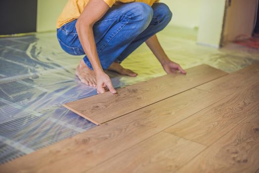 Man installing new wooden laminate flooring on a warm film floor. infrared floor heating system under laminate floor