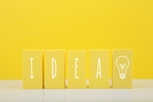 Concept of idea, creativity, start up or brainstorming. The word idea and bulb drawn on yellow toy blocks against bright yellow background with copy space.