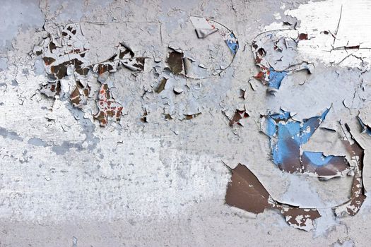 Light coloured paint peels and cracks off of a metal surface showing a brown colour beneath. The paint is heavily cracked and weathered.