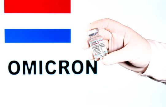 Madrid, Spain- November 29, 2021: Hand holding vial with Moderna covid vaccine. Dutch flag and Omicron covid variant word written in the background