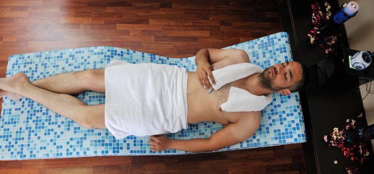 young beautiful man relaxing at spa and wellness center at hot bed with blue tiles decoration