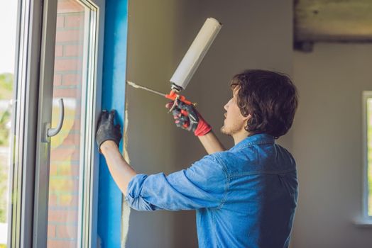 Man in a blue shirt does window installation. Using a mounting foam.
