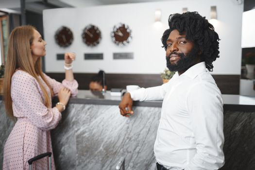 Business trip concept. Black man and caucasian woman businesspeople colleagues checking-in in hotel reception desk