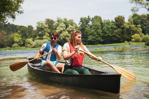 Couple adventurous explorer friends are canoeing in a wild river surrounded by the  beautiful nature