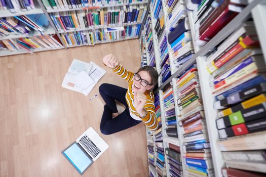 student taking notes from a book at library. Young woman sittingin in school library and working with laptop