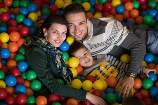 Happy young parents are playing with their kids at pool with colorful balls in a children's playroom