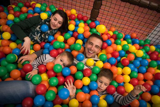 Happy young parents are playing with their kids at pool with colorful balls in a children's playroom