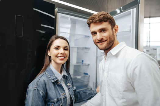 Young couple selecting new refrigerator in household appliance store, close up