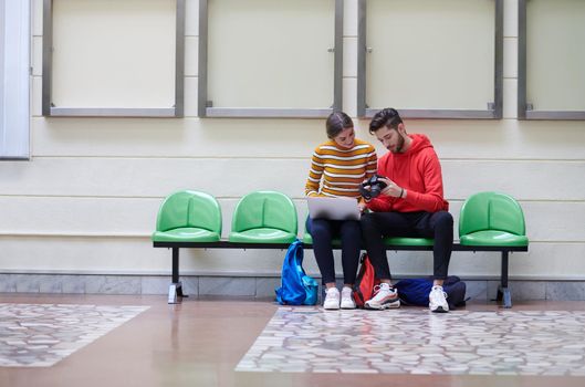 two students sit in the school hallway and use notebooks, tablets and cameras to create projects for the school