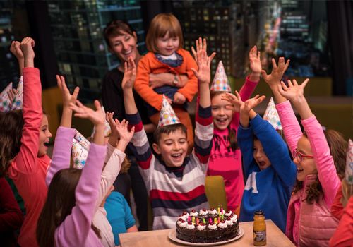 young happy boy and group of his friends having birthday party with a night city through the windows in the background
