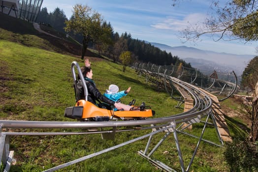 young excited mother and son enjoys driving on alpine coaster